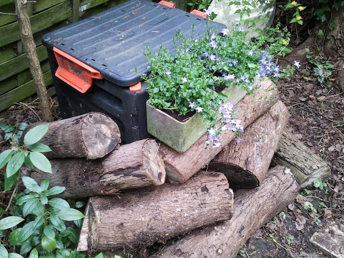 My home compost barrel, hidden behind some logs and plants.